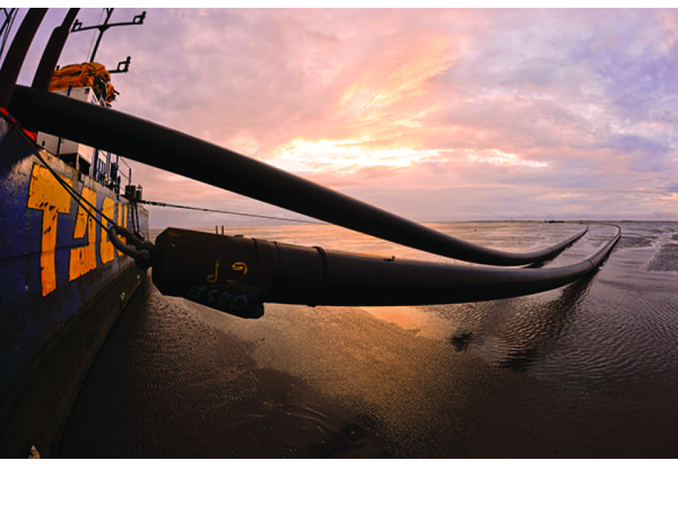 This image shows submarine HVDC (High Voltage Direct Current) cables being installed or laid from a vessel onto a coastal area or shallow seabed.